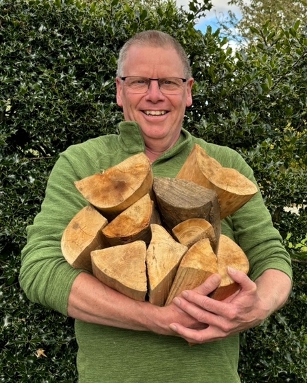 Chris standing outside, holding a pile of cut logs