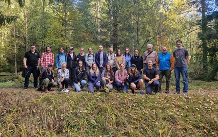 22 people stand or kneel outside in a forest